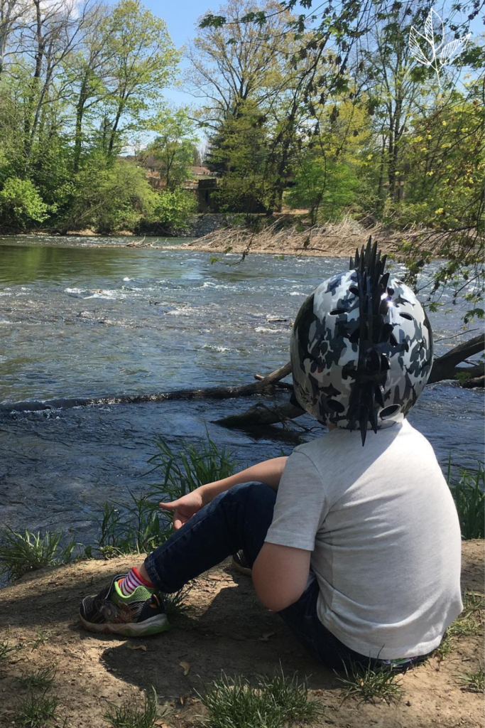 my son sits on ground overlooking our local creek