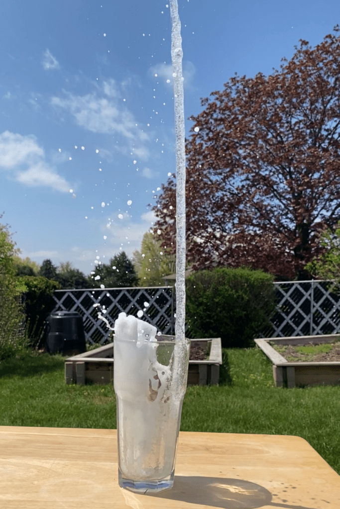 Plastic water bottle propelled out of the frame of the picture, leaving only a trail of water shooting vertically out of the bottle. 