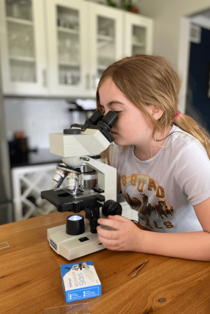 girl is using trinocular microscope to look at a prepared slide.
