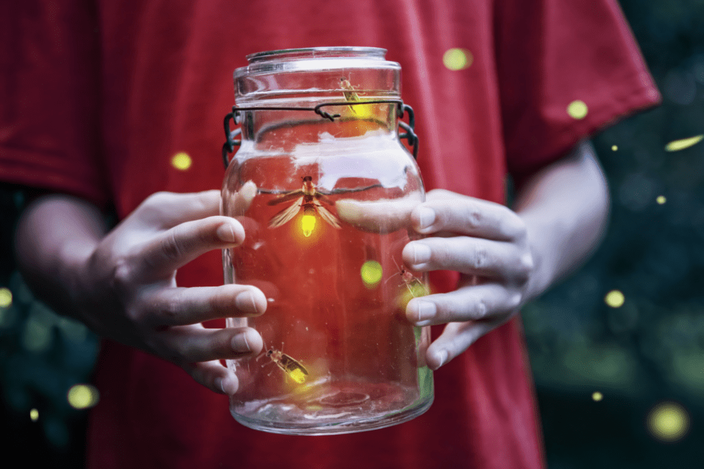 Child holds a glass jar that contains glowing fireflies