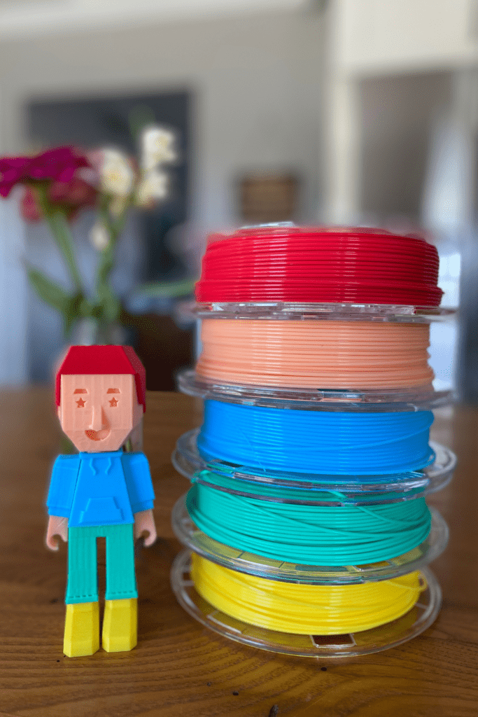 A 3D printed toy stands next to a stack of printer filament