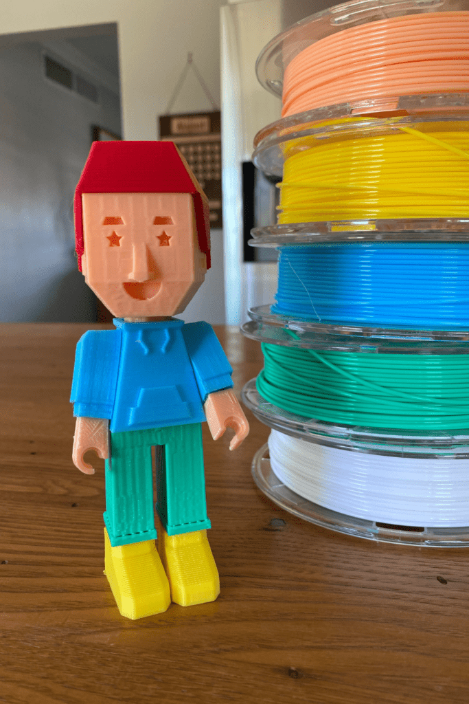 A 3D printed toy stands next to a stack of printer filaments.