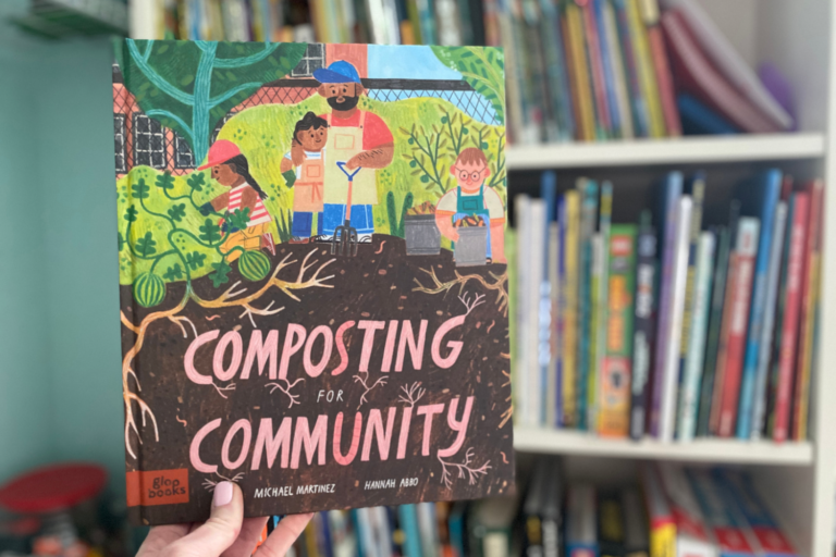 Hand holds up the book, Composting for Community, in front of a bookshelf background.
