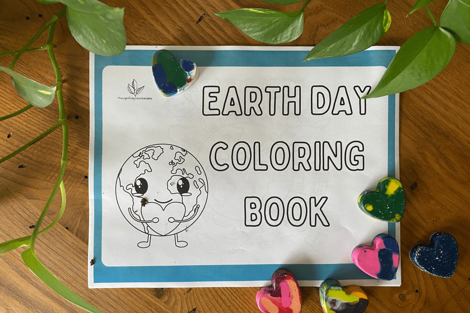 Earth Day Coloring Book sits on a wooden table with a green plant and some upcycled heart crayons